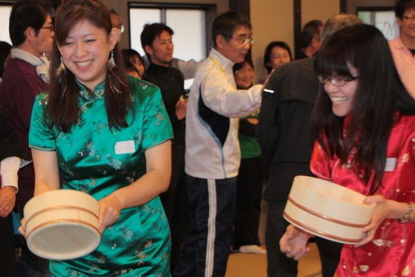 緑と赤のチャイナドレスを着た女性2人が桶を持って笑っている写真